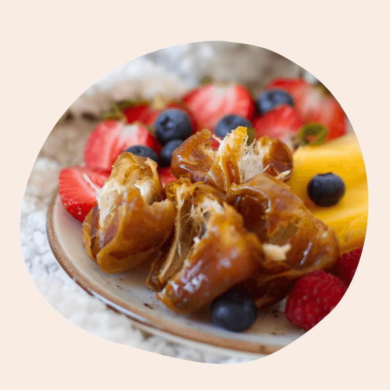 Aufgebrochene, weiche Datteln angerichtet auf einem Teller zusammen mit frischen Erdbeerscheiben, Heidelbeeren, Himbeeren und Mango.