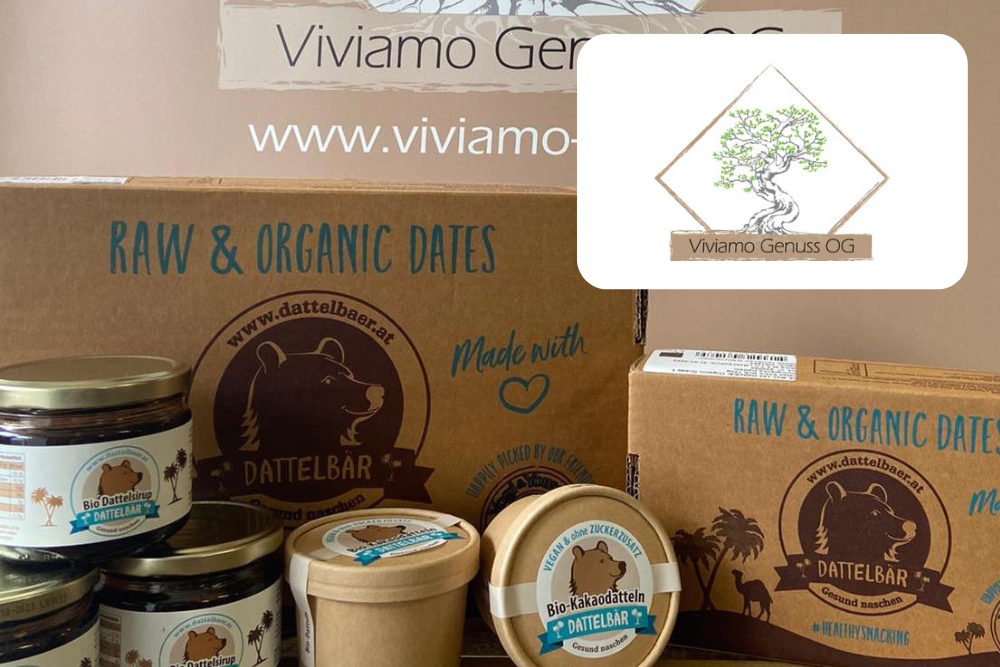 Eine Auslage mit Bio-Dattelprodukten der Marke Dattelbär in Gläsern und Schachteln, mit dem Logo der Viviamo Genuss OG und der Website im Hintergrund.