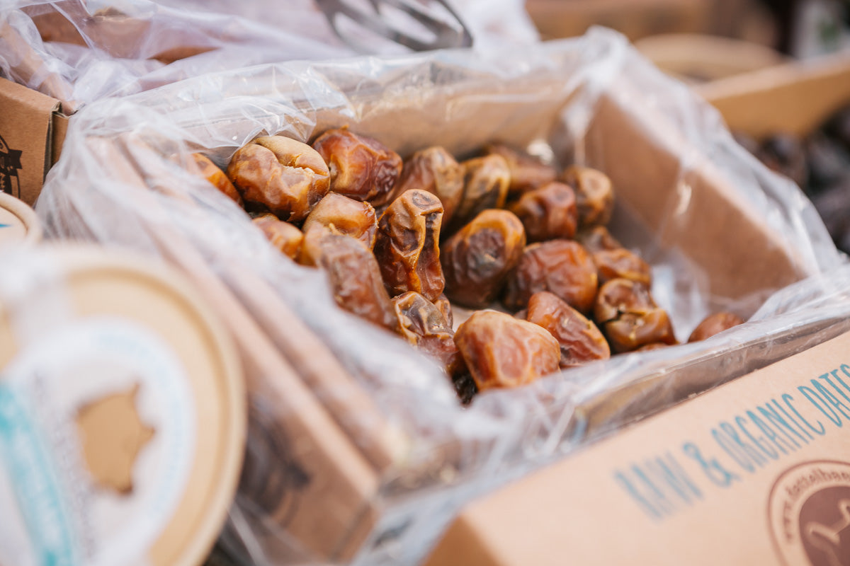 Nahaufnahme einer mit getrockneten Datteln gefüllten Pappschachtel, die mit durchsichtigem Plastik ausgekleidet ist. Andere verpackte Produkte sind teilweise um die Schachtel herum sichtbar.